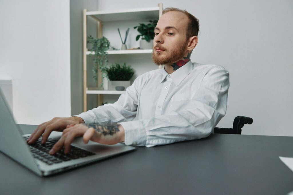 A man in a wheelchair a businessman with tattoos in the office works at a laptop, integration into